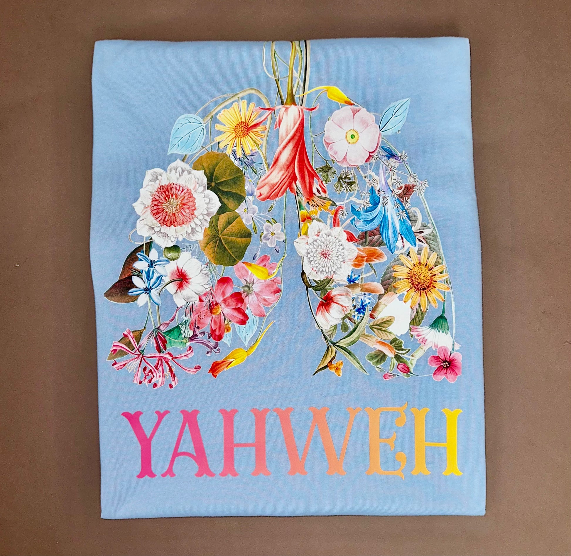 YAHWEH Bloom Premium Tee featuring colorful floral design on a light blue fabric.